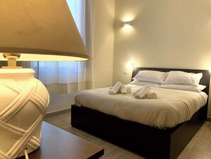 A neatly made bed with white linens and rolled towels, a bedside lamp, and a wall-mounted light fixture. - Double room with private bathroom in Terralba  (Oristano) - Helichrysum (Terralba)