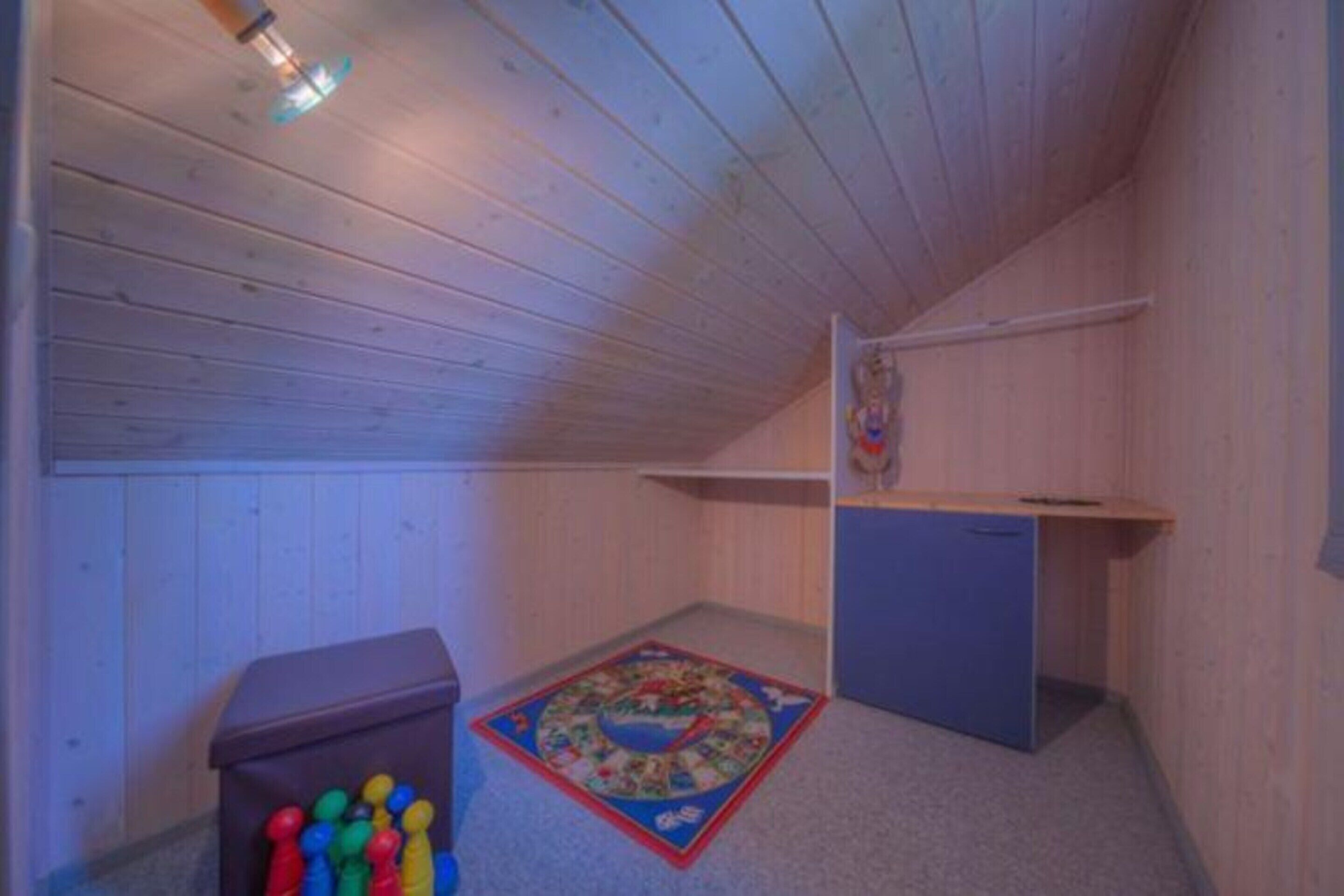 A small, wooden-paneled room with a sloped ceiling, a blue carpet, and a small desk.