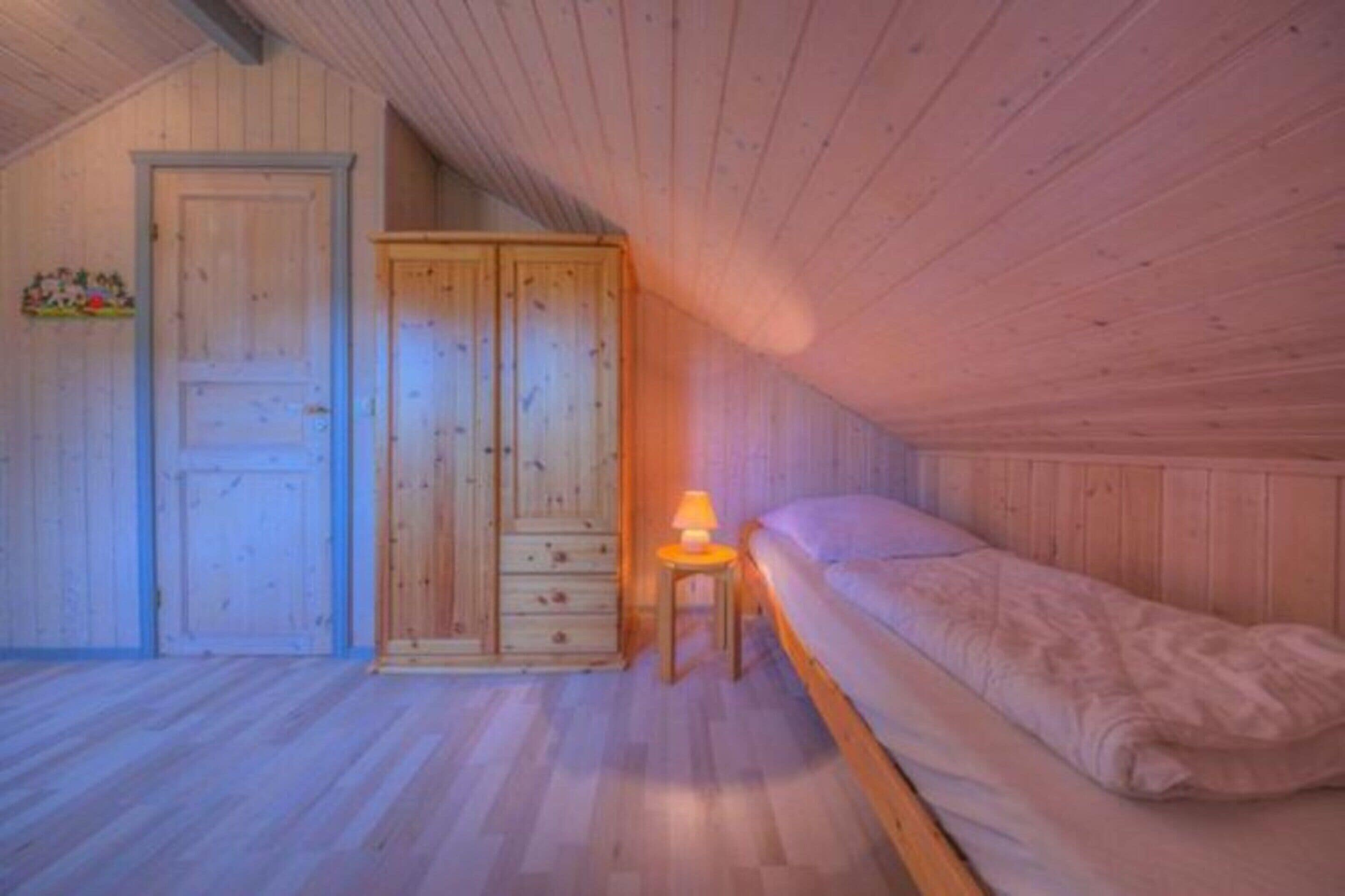 A bedroom with a wooden ceiling, a bed, a wardrobe, and a nightstand with a lamp.