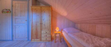 A bedroom with a wooden ceiling, a bed, a wardrobe, and a nightstand with a lamp.