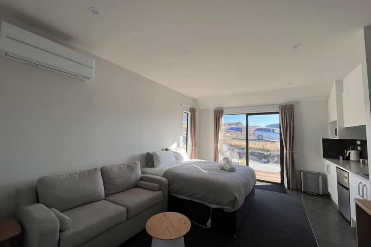 Une chambre d’hôtel moderne équipée d’un canapé, d’un lit, d’une petite table ronde, d’un coin cuisine et d’une grande fenêtre donnant sur un paysage agréable.