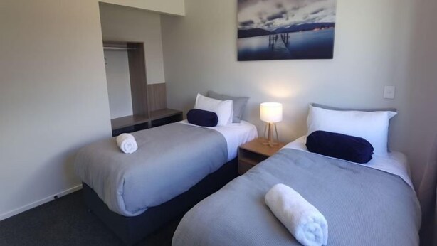A hotel room with two beds, a nightstand, a lamp, and a painting on the wall. - Sky Valley (Lake Tekapo)