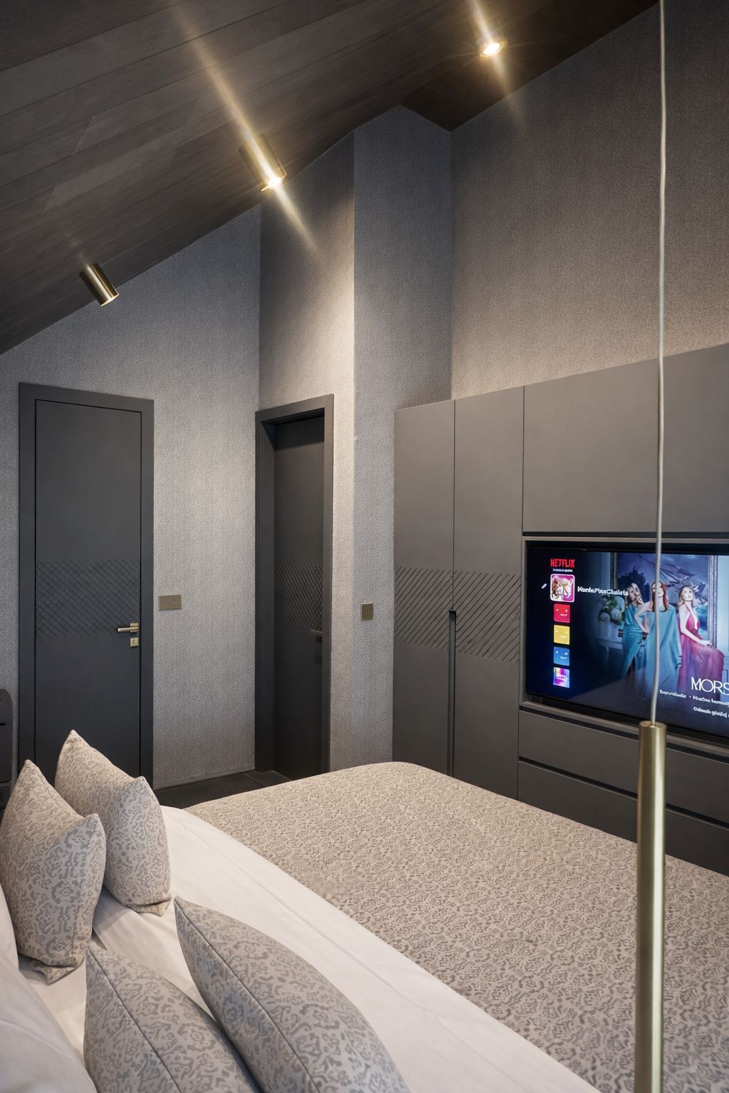 Een moderne slaapkamer met een groot bed, een aan de muur bevestigde televisie en een deur naar een andere kamer.