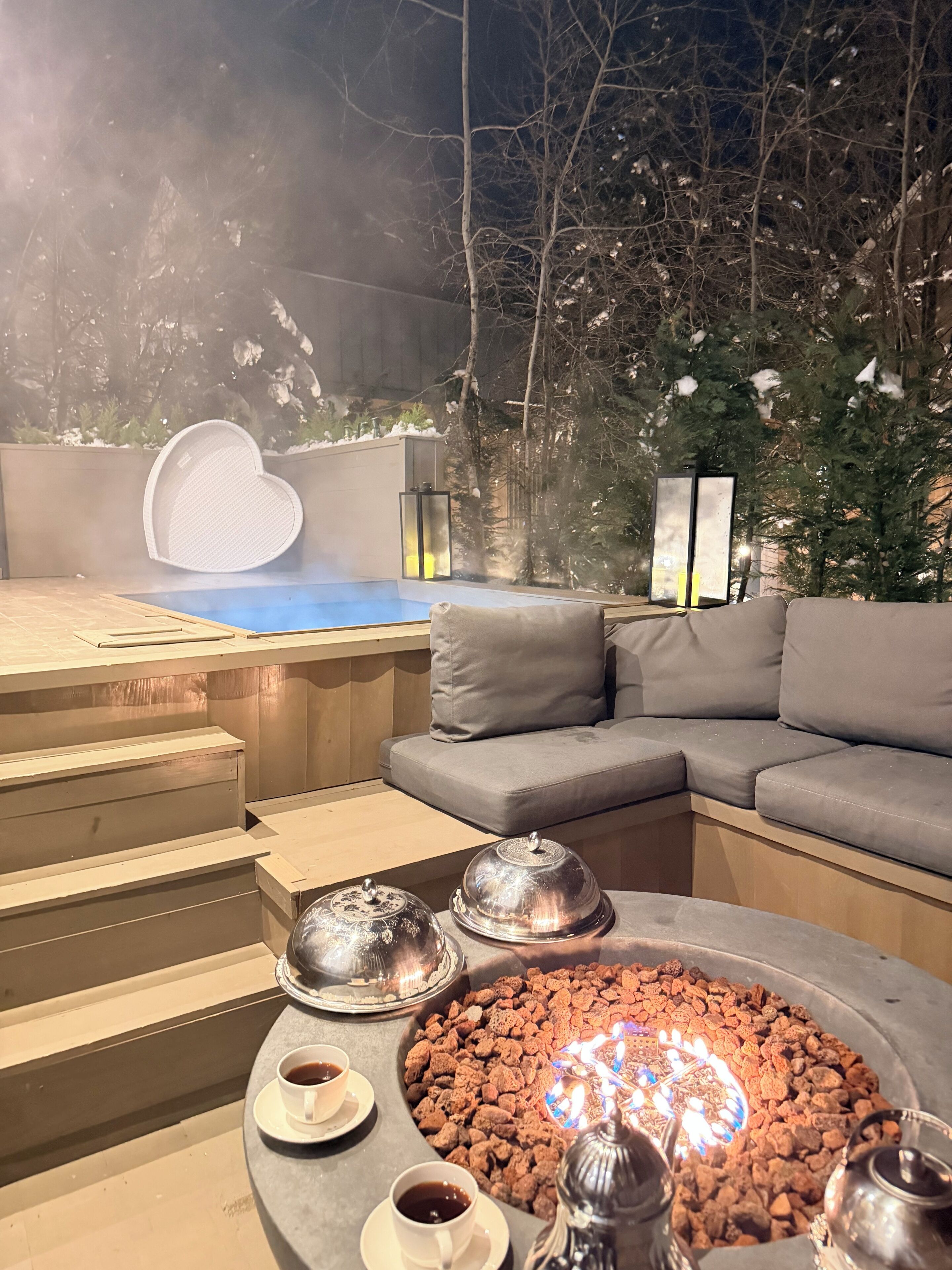 A cozy outdoor seating area with a fire pit, cushions, and a heart-shaped decoration.
