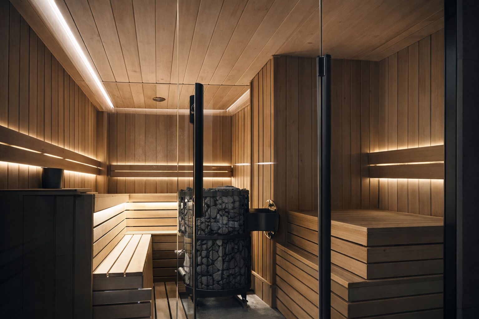 Een sauna met houten banken en een stenen kachel, met warme verlichting en houten wandbekleding.