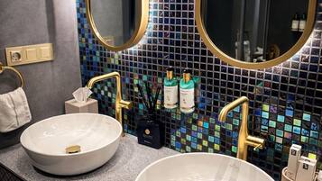A bathroom with two round white sinks, gold faucets, and a mosaic tile backsplash.