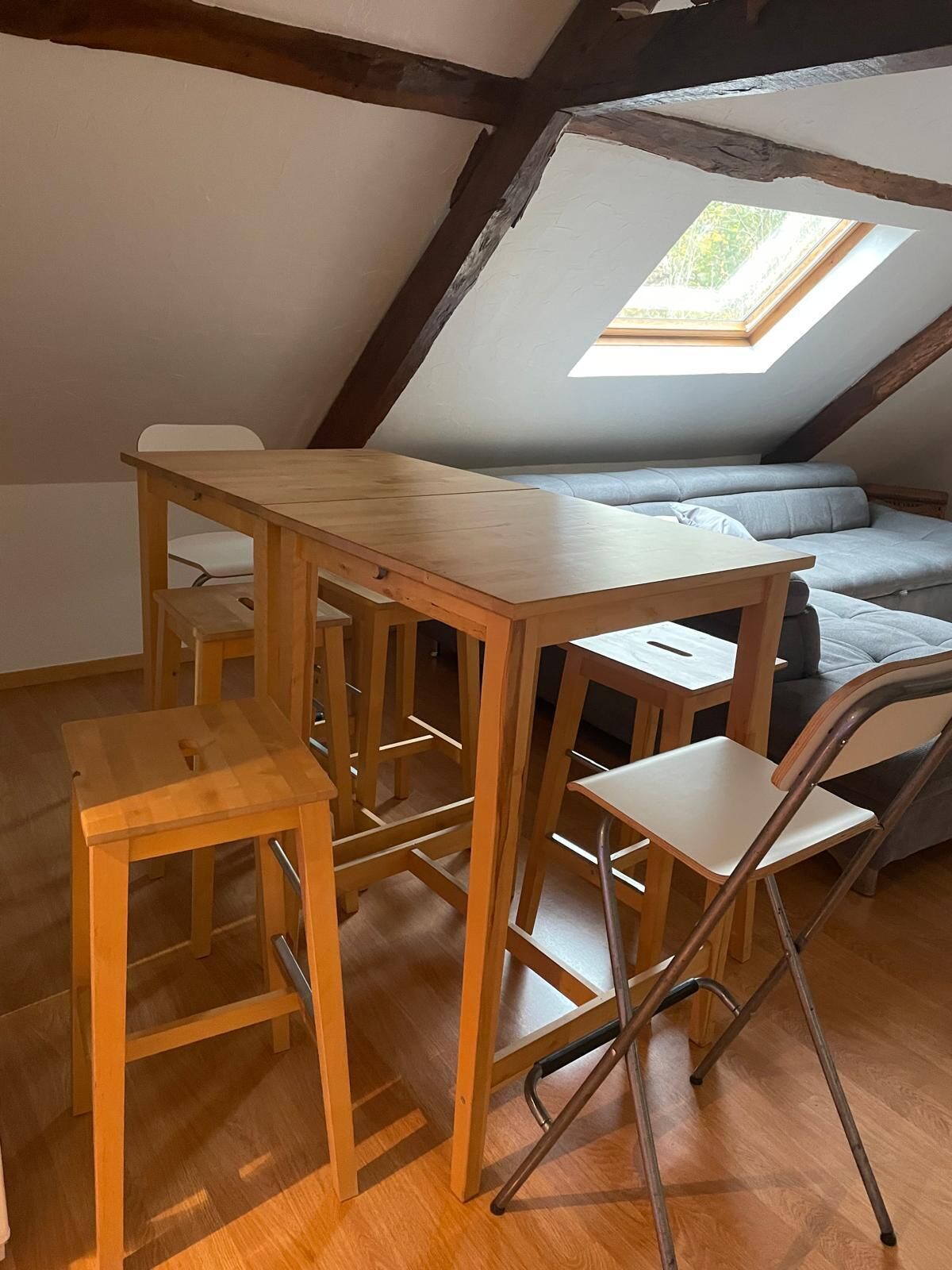 Habitación tipo loft con una mesa de comedor de madera, dos sillas, un sofá y un tragaluz.