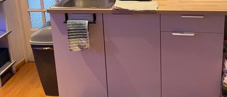 Cocina compacta con lavamanos, microondas y escurreplatos. Hay una ventana con diseño de vidrio texturizado y una toalla colgando del armario.