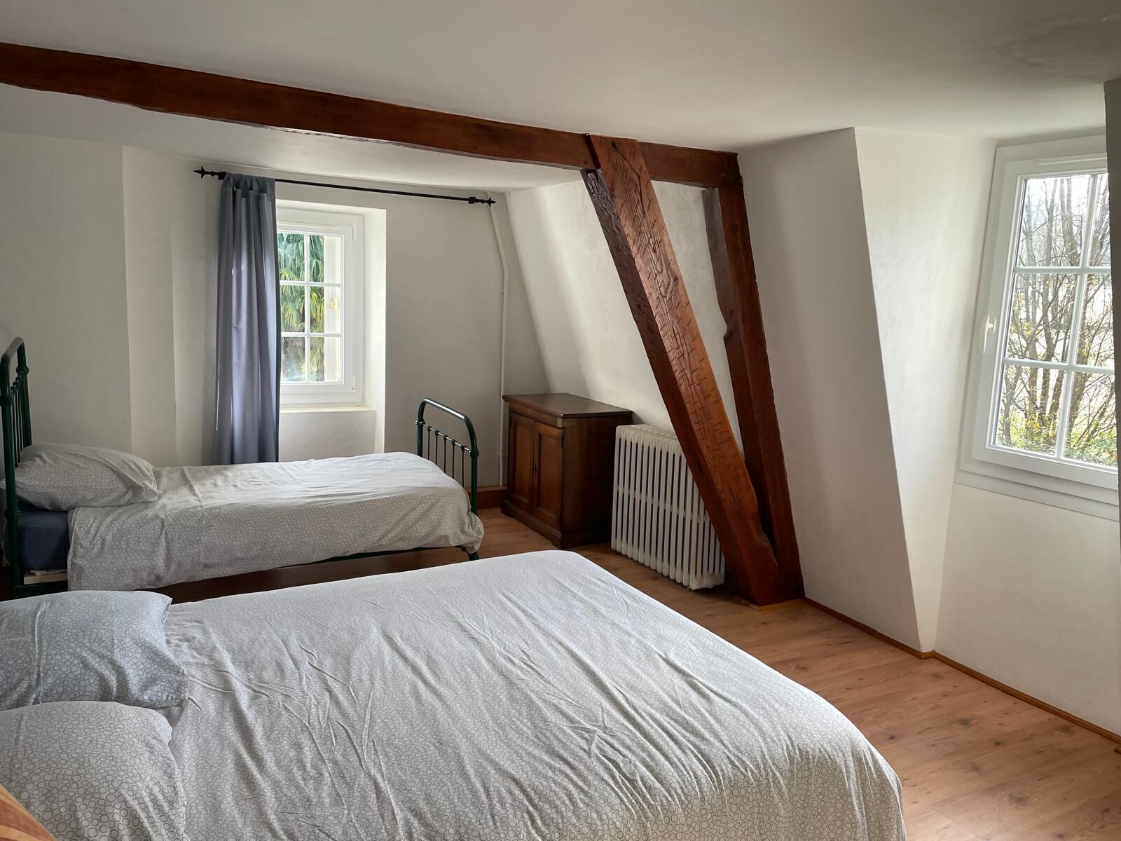 Un dormitorio con dos camas, una ventana, un radiador y vigas de madera a la vista.