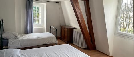 Un dormitorio con dos camas, una ventana, un radiador y vigas de madera a la vista.