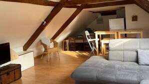 A cozy attic room with exposed wooden beams, a gray sofa, a wooden dining table, and a television. - La Caminade (Bourg-de-Bigorre)