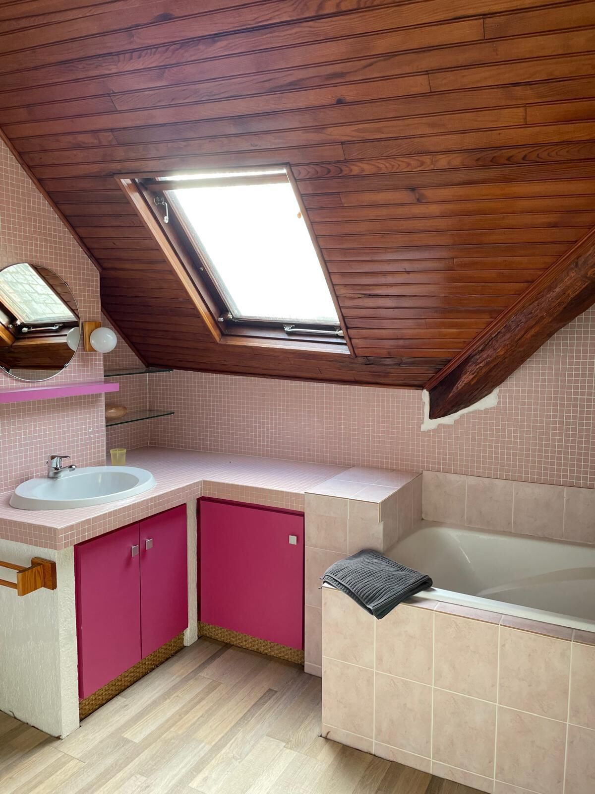 A small, sloped-roofed bathroom with a skylight, pink cabinets, a white sink, and a bathtub.