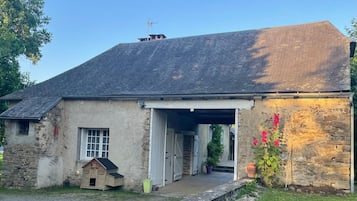 Un bâtiment rustique en pierre, doté d’un toit en pente, d’un porche abrité et d’une petite maisonnette en bois servant de jeu.