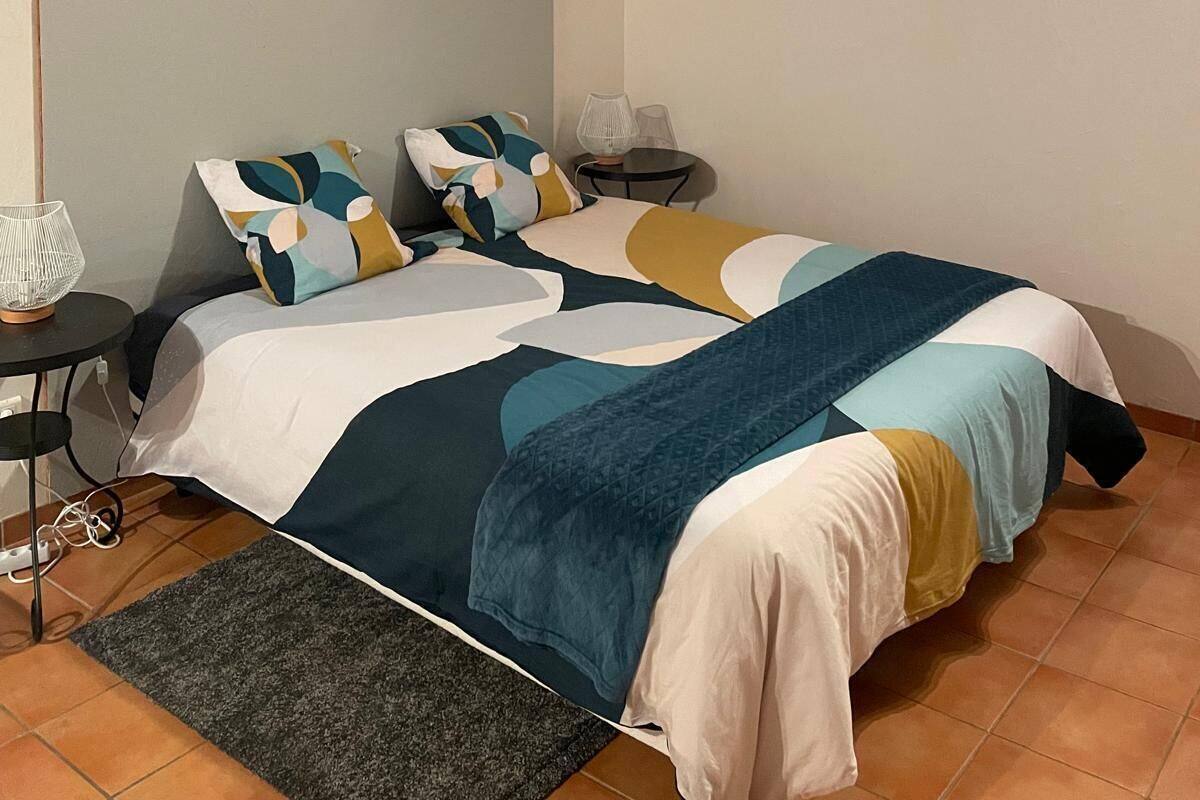 Ein Schlafzimmer mit Bett, Kissen, einem kleinen Tisch mit Lampe und einem Teppich.