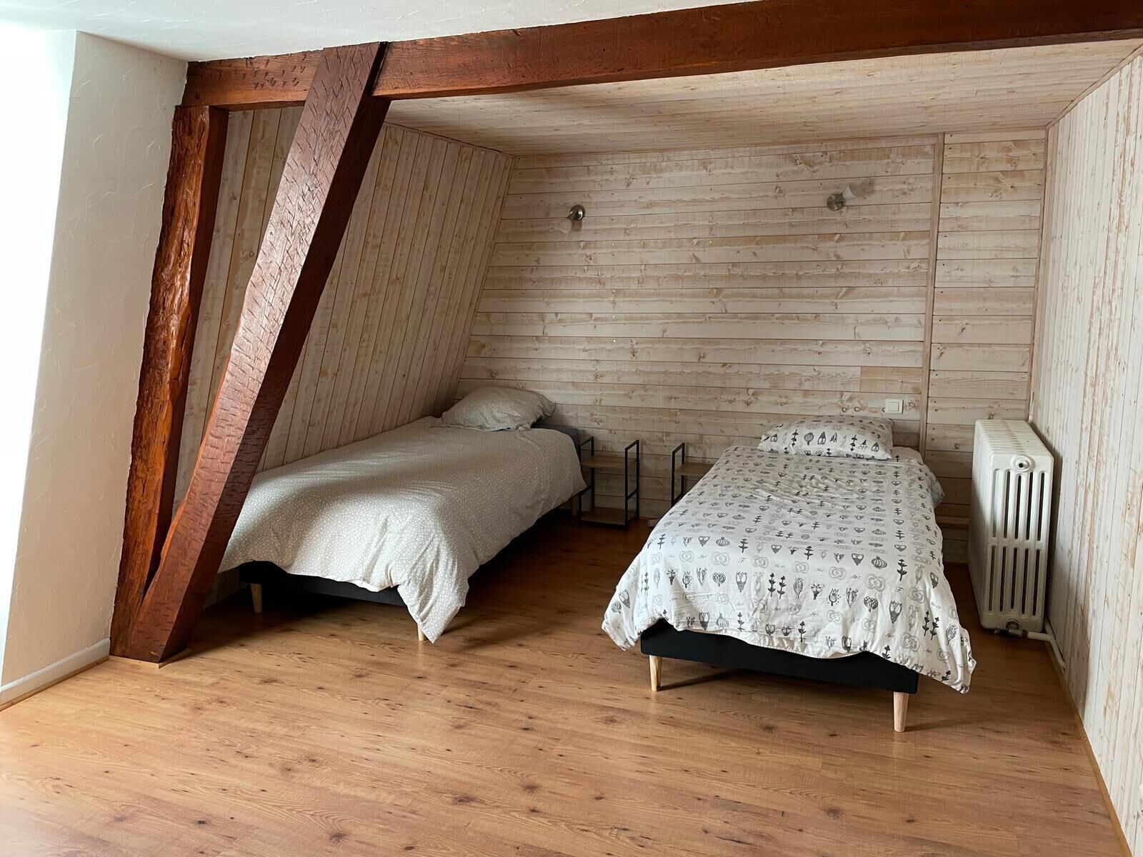 A small, cozy attic bedroom with two beds, wooden beams, and a radiator.