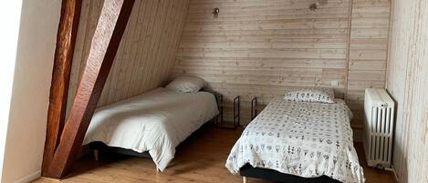 A small, cozy attic bedroom with two beds, wooden beams, and a radiator.