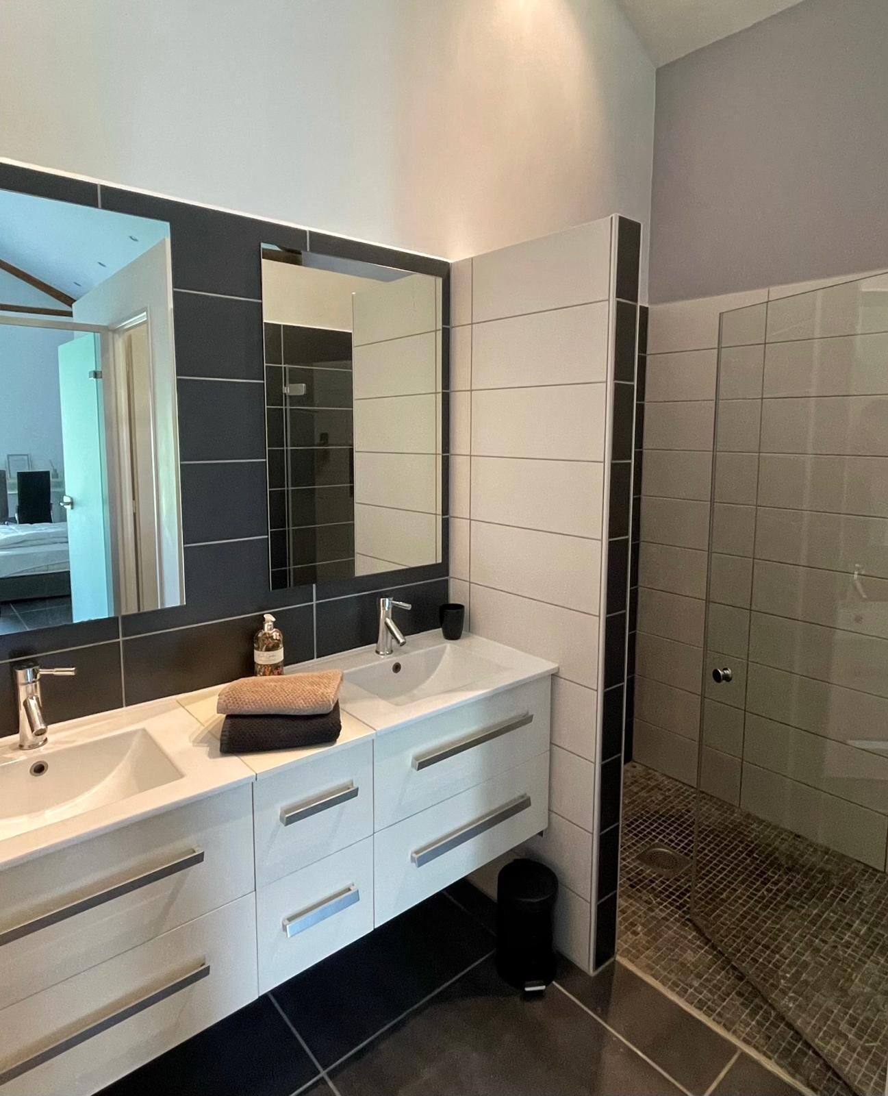 A modern bathroom with a large mirror, two sinks, and a shower area.