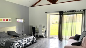 A modern bedroom with a large bed, a desk, and a sofa. There is a sliding glass door leading to a balcony. - La Caminade (Bourg-de-Bigorre)