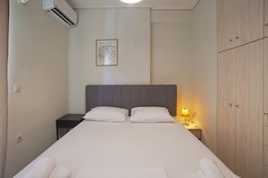 Una cama bien tendida con sábanas blancas, una lámpara de noche y un cuadro en la pared.
