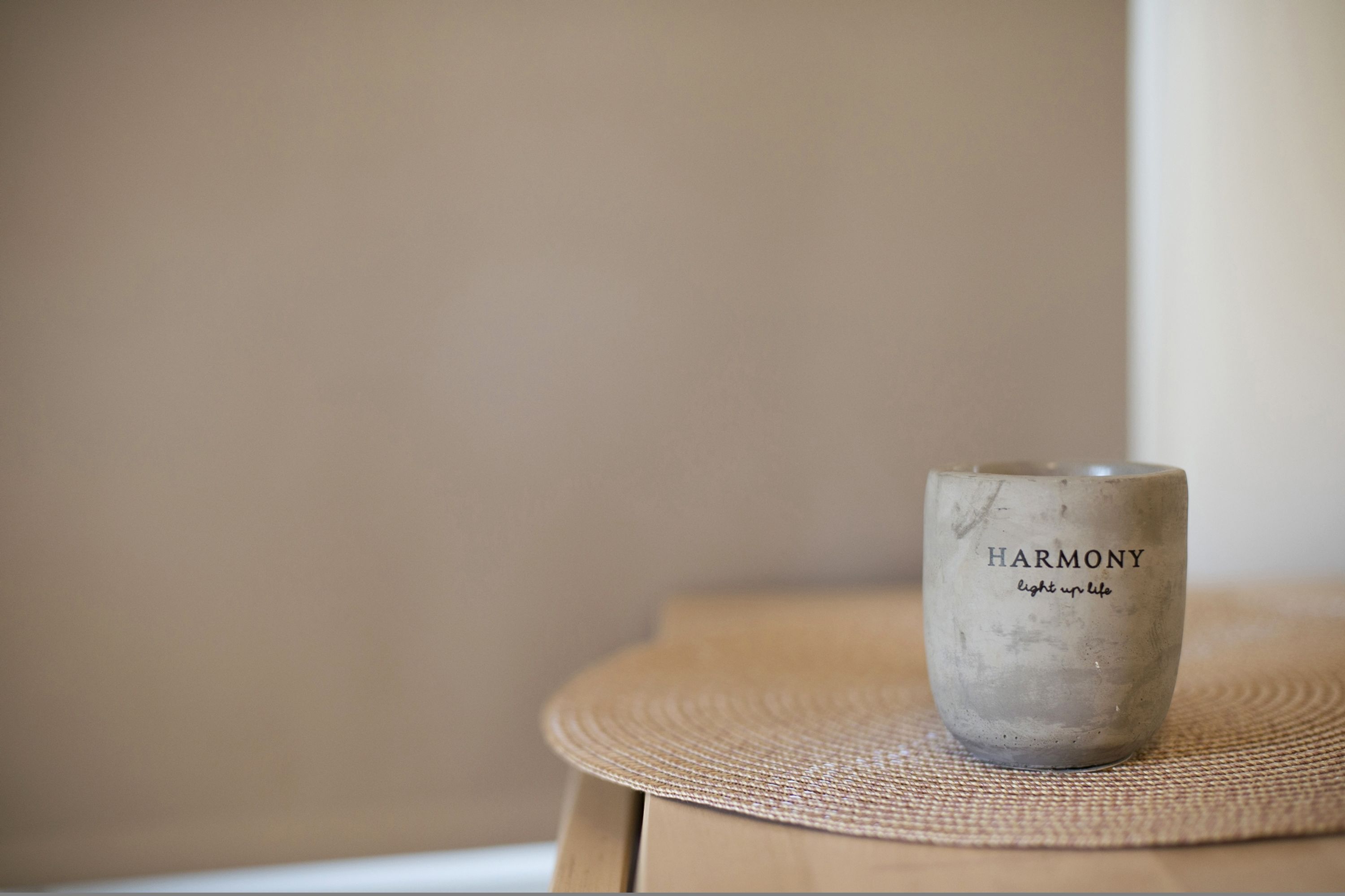 A candle with the words "HARMONY" and "light up life" on it, placed on a woven mat on a wooden surface.
