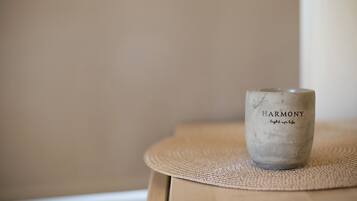 A candle with the words "HARMONY" and "light up life" on it, placed on a woven mat on a wooden surface.
