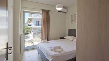 A bedroom with a bed, a nightstand, a hanging light, a window with a curtain, and an air conditioning unit.