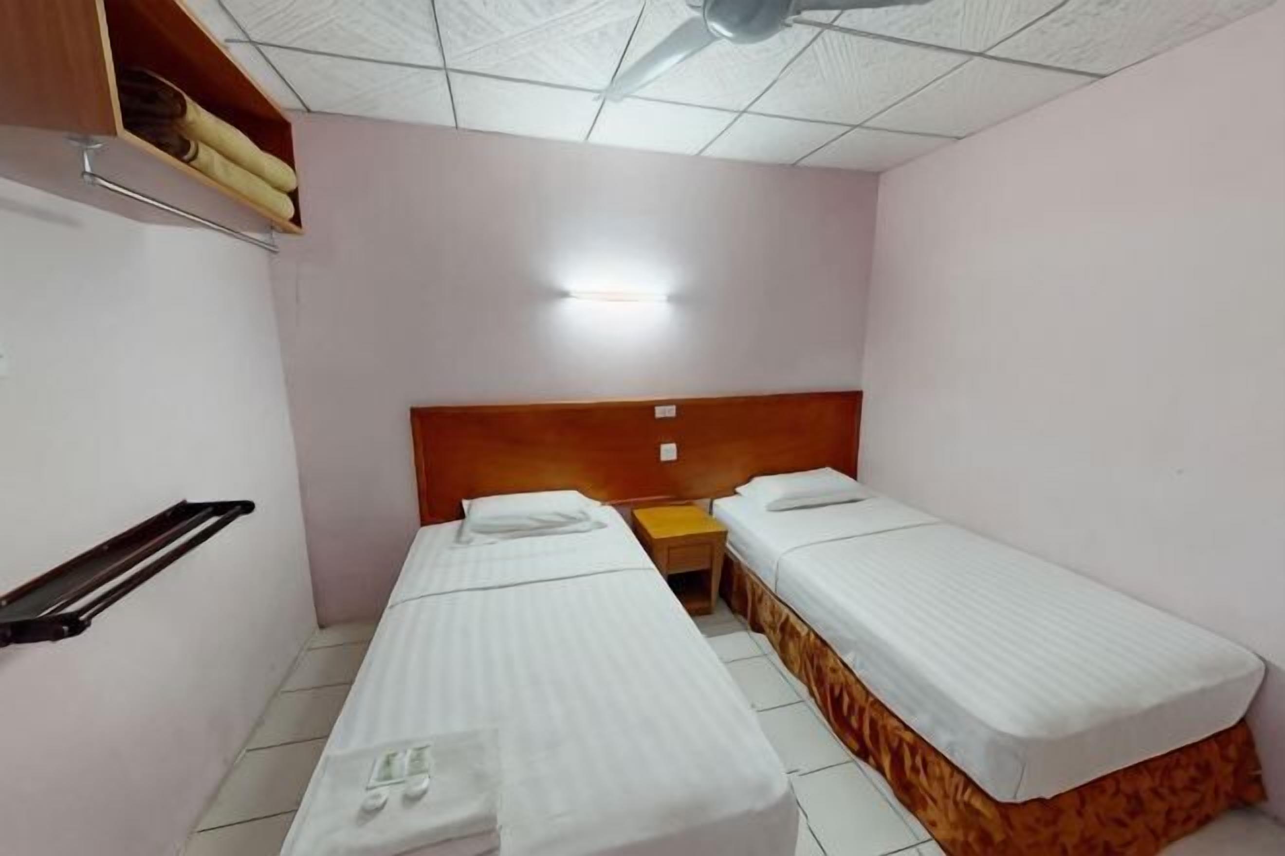 Ein Zimmer mit zwei Einzelbetten, einem Holz-Kopfteil, einem kleinen Tisch und einem Deckenventilator.