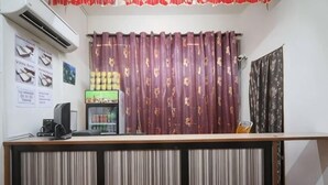 Un comptoir d’accueil équipé d’un ordinateur, d’un réfrigérateur à boissons et d’une fenêtre avec des rideaux.
