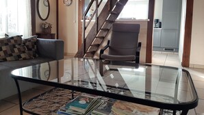 Un salon avec une table basse en verre, un canapé, un fauteuil et un escalier.