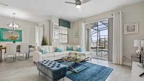 A modern living room with a sofa, ottoman, coffee table, and a dining area with chairs.