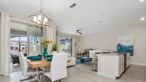 A spacious living area with a dining table, white chairs, a sofa, a kitchen island, and a ceiling fan.