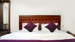 Ein Hotelzimmer mit einem großen Bett, zwei violetten Kissen, einem Holz-Kopfteil und einem Nachttischchen mit Telefon.