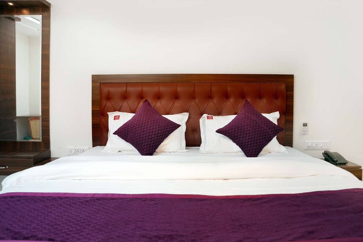 A hotel room with a large bed, two purple pillows, a wooden headboard, and a bedside table with a phone.