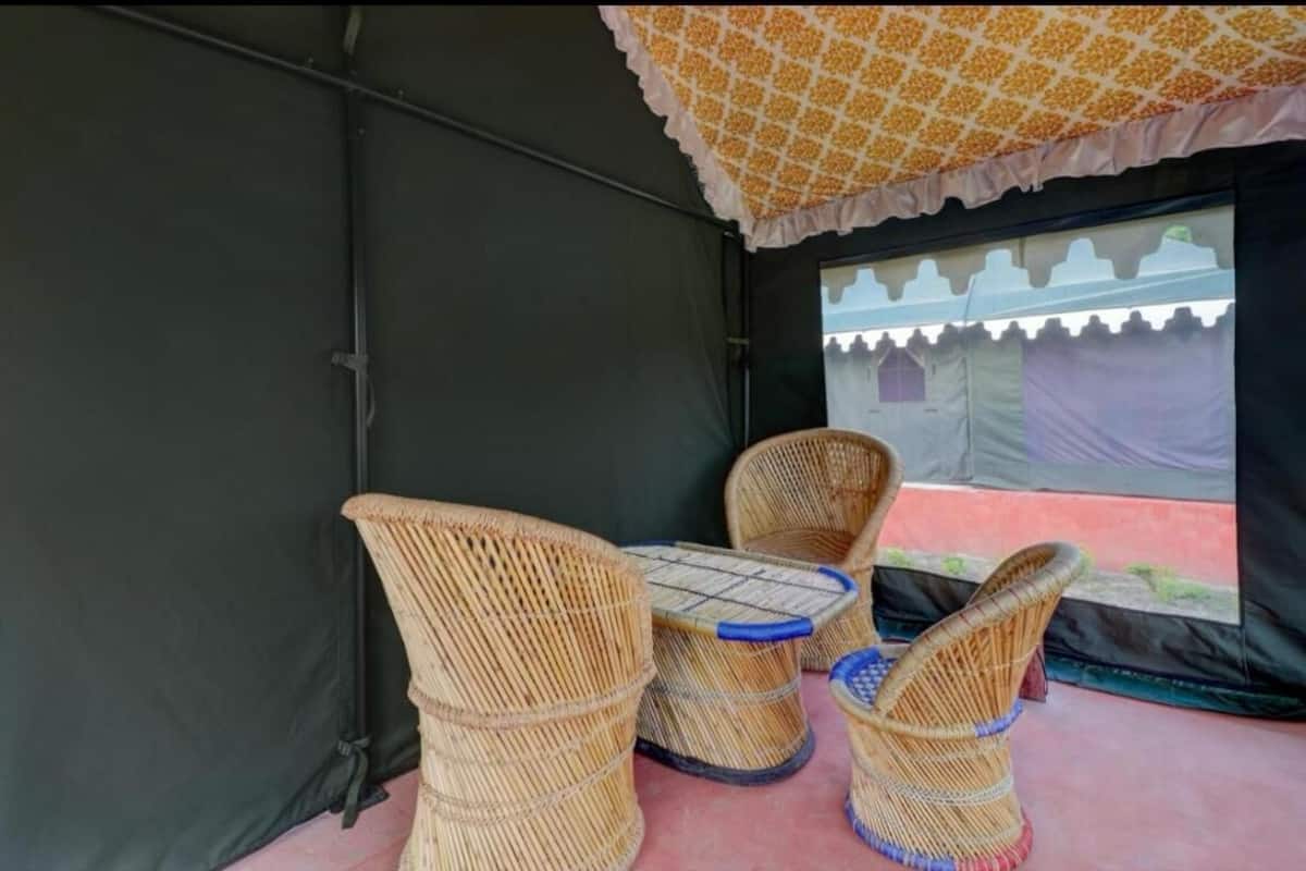 Un espace aménagé sous une tente, avec des meubles en osier et une vue sur un bâtiment traditionnel situé à l’extérieur.