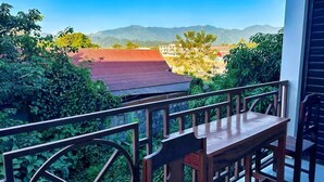 Un balcón con una mesa y sillas de madera, con vista a un paisaje montañoso y edificios a lo lejos.