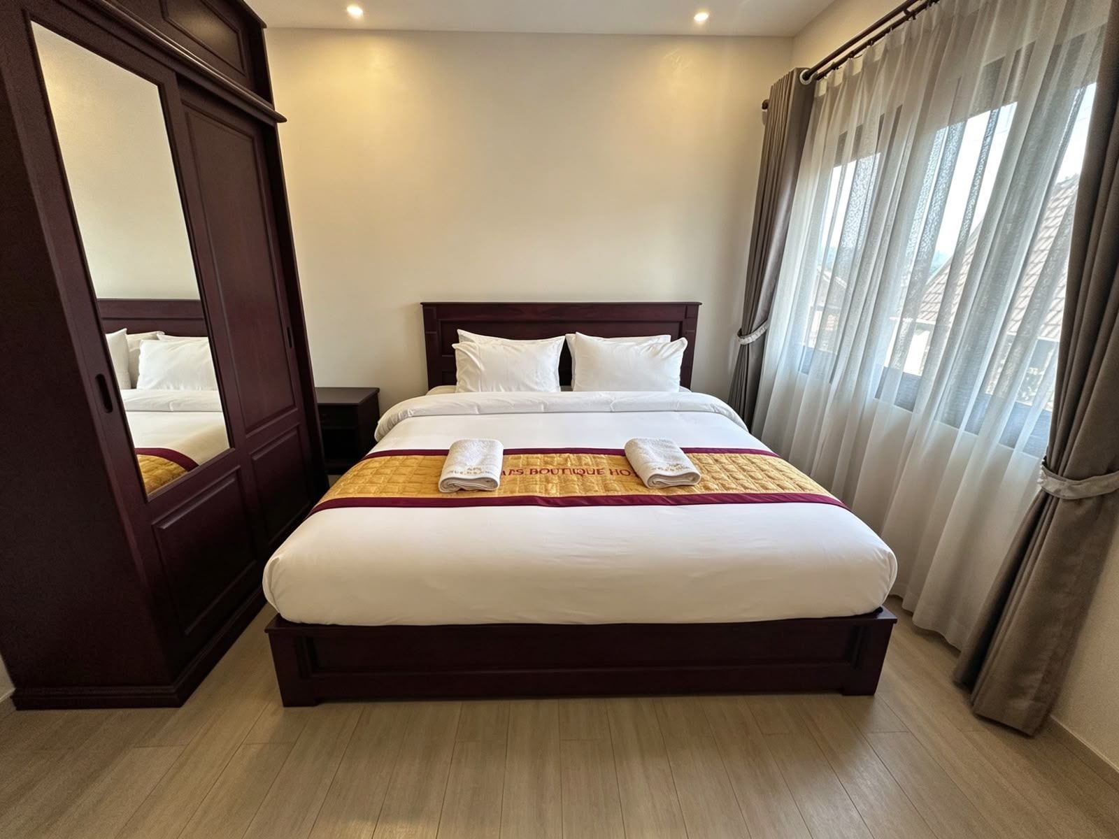 A hotel room with a large bed, a wardrobe, and a window with curtains.