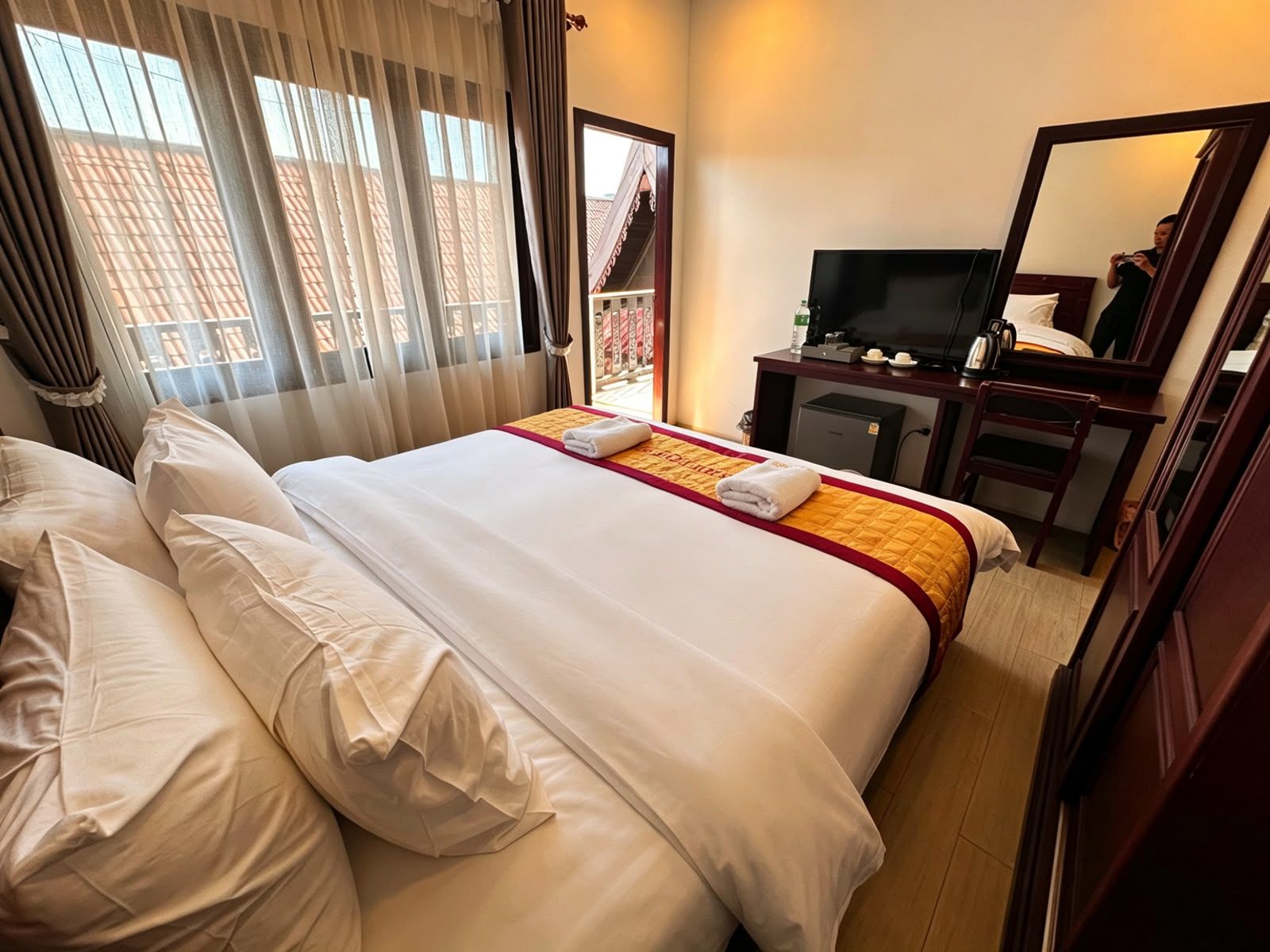 A hotel room with a large bed, a television, a desk with a chair, and a window with curtains.