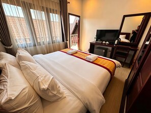 A hotel room with a large bed, a television, a desk with a chair, and a window with curtains. - A P S Boutique Hotel (Vang Vieng)