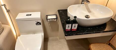 Un baño con inodoro, lavabo, espejo y dispensador de gel antibacterial.