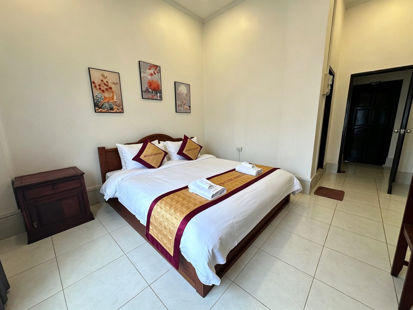 A hotel room with a large bed, a wooden nightstand, and a door leading to another room.