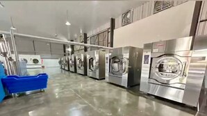 Un lavadero industrial con varias lavadoras de acero inoxidable alineadas sobre un piso de concreto pulido.