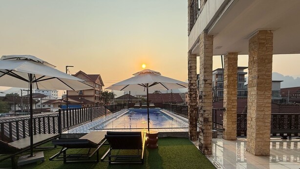 Un área de piscina en la azotea con sillones y sombrillas, rodeada de pilares de piedra y vistas al atardecer.