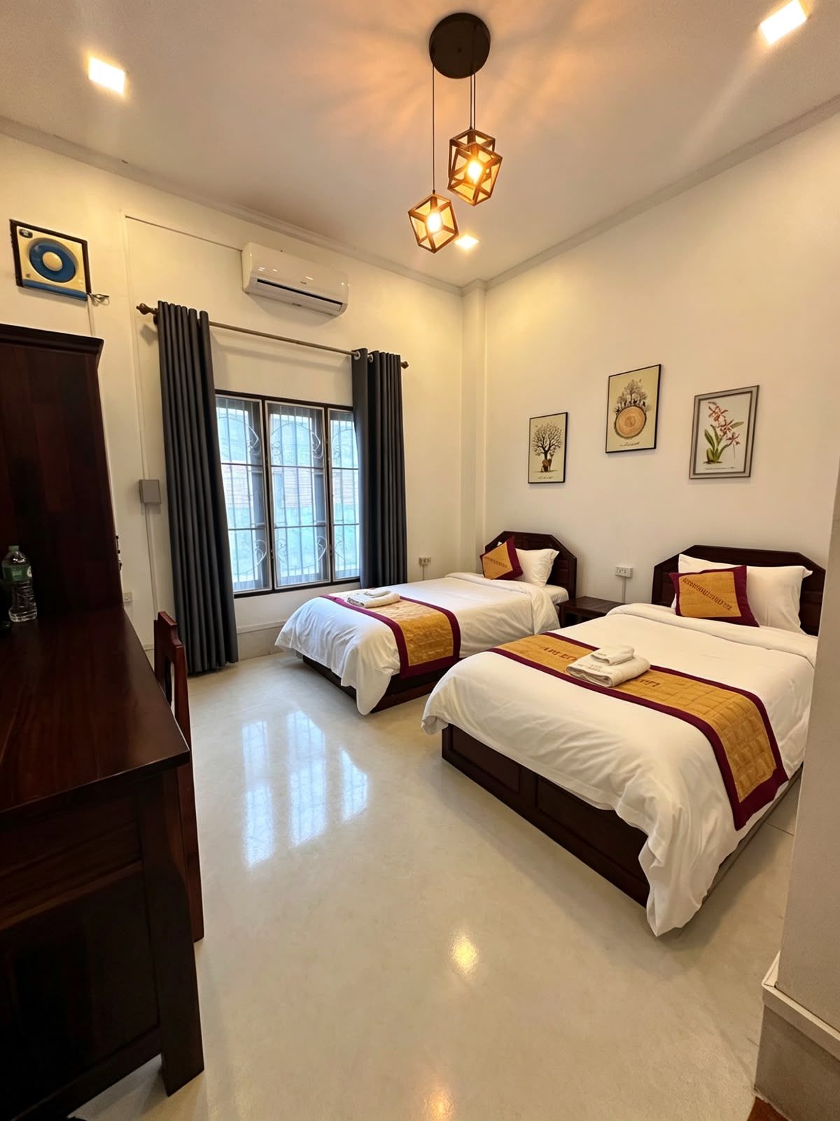 A hotel room with two beds, a wooden desk, a window with curtains, and wall-mounted artwork.