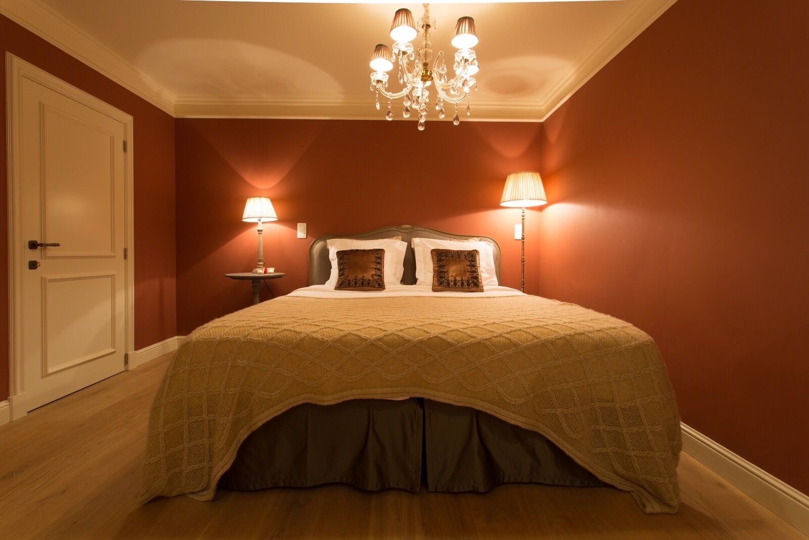 A bedroom with a large bed, two bedside lamps, a chandelier, and a door.