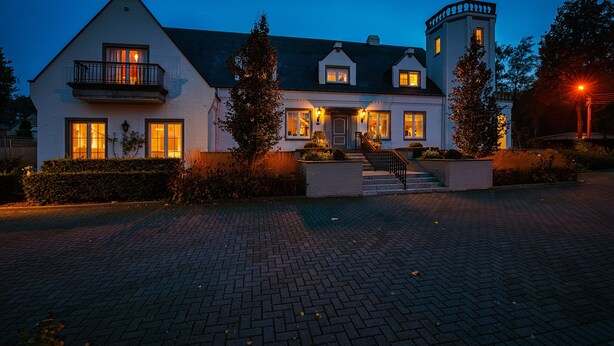 A large, two-story house with a tower, a balcony, and a well-lit entrance. - Villa Reynaert (Maaseik)