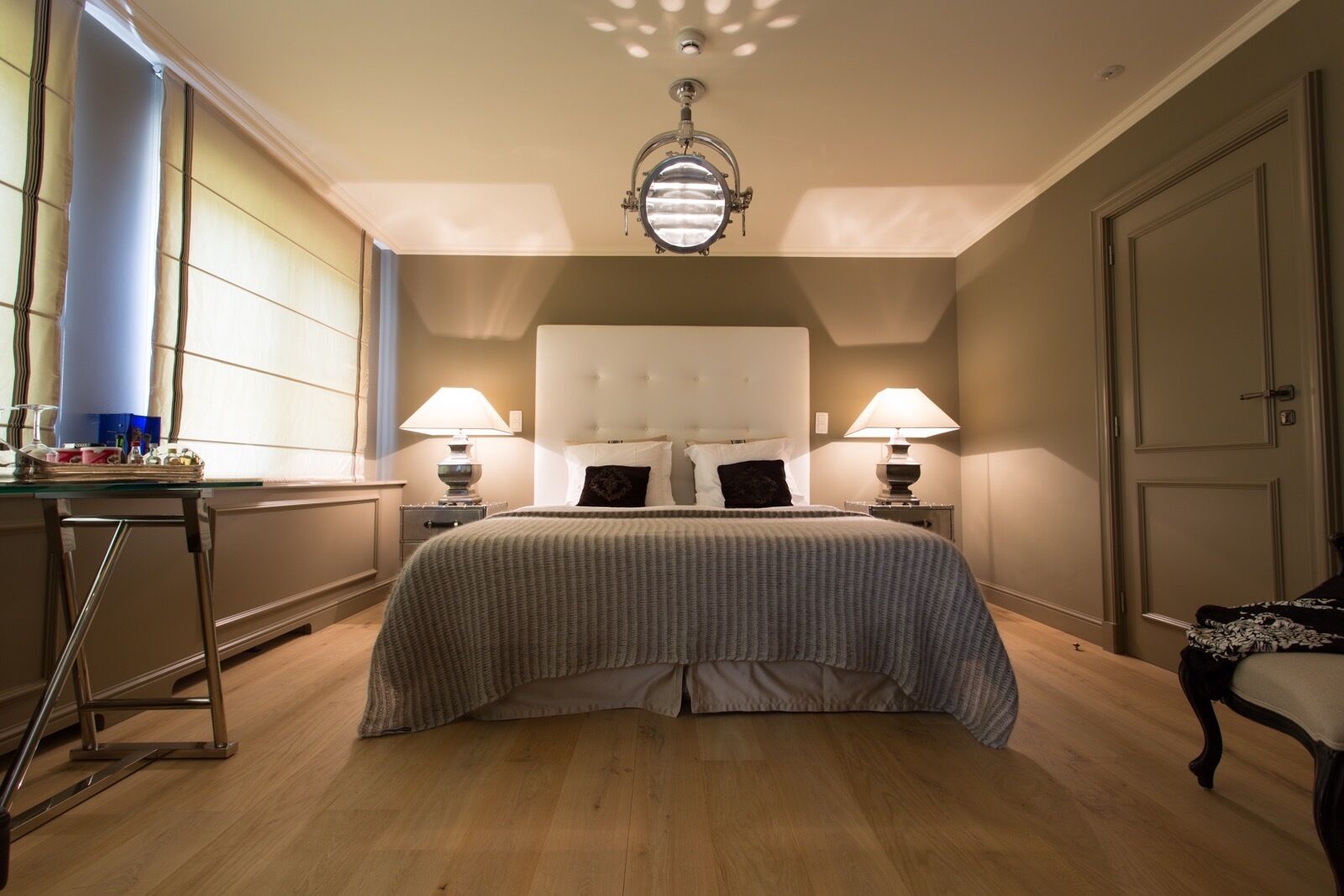 Une chambre d’hôtel avec un grand lit, deux tables de chevet avec des lampes, un bureau avec une chaise et une grande fenêtre avec des rideaux.