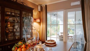 A well-lit room with a wooden buffet table, a glass cake stand, and a dining area with a view through glass doors. - Villa Reynaert (Maaseik)