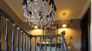 A grand staircase with a chandelier, a mounted ram's head, and a book on a console table. - Villa Reynaert (Maaseik)