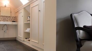 Une salle de bain avec un meuble-lavabo blanc, un miroir, un porte-serviettes et une étagère contenant des articles de toilette.