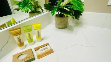 A bathroom with a white marble countertop, a potted plant, and three bottles of ESSENCE body lotion.